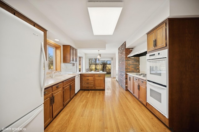 kitchen with white appliances, brown cabinetry, light wood finished floors, a peninsula, and light countertops