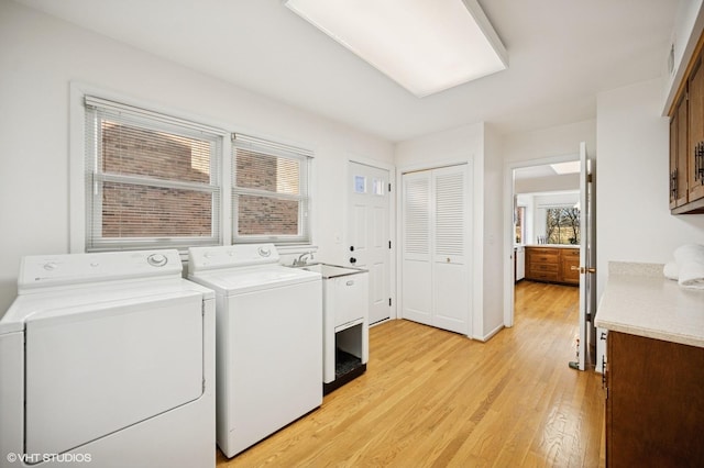 laundry room with a wealth of natural light, light wood-type flooring, a sink, and washing machine and clothes dryer