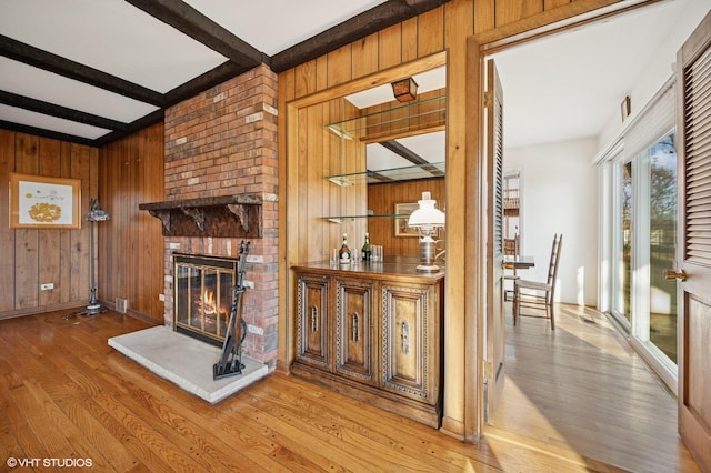 living room featuring beam ceiling, wood finished floors, a fireplace, and wood walls