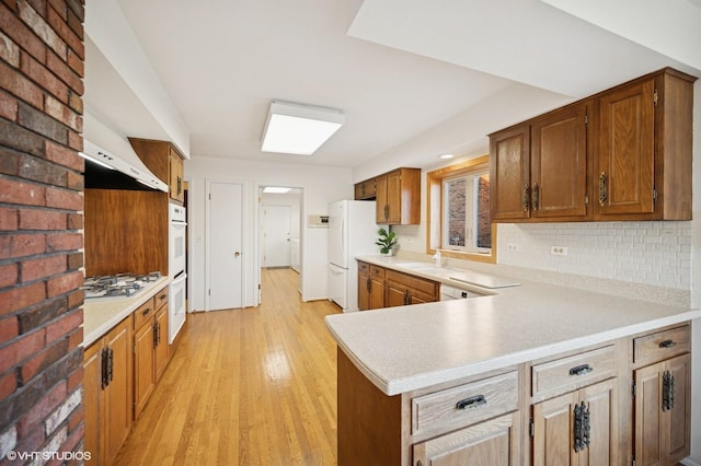 kitchen with decorative backsplash, white appliances, light countertops, and light wood-style floors