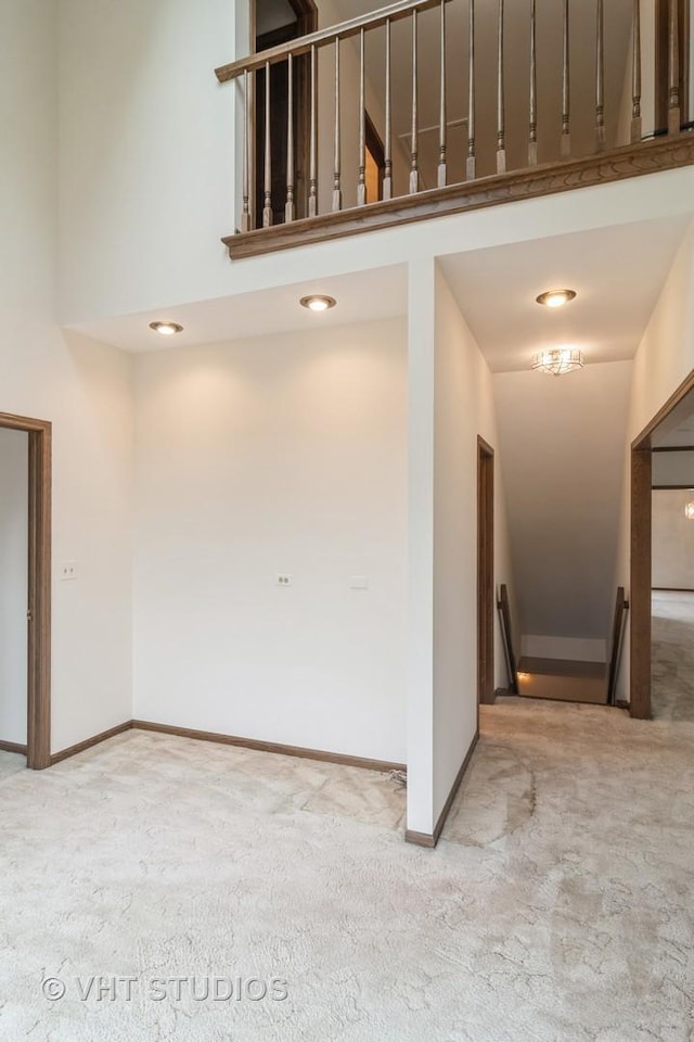 carpeted spare room featuring a high ceiling and baseboards