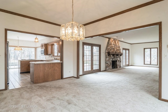 kitchen with ornamental molding, brown cabinetry, a stone fireplace, and light colored carpet