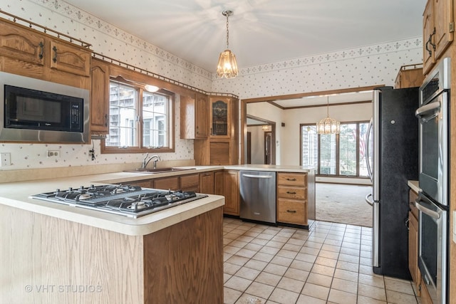 kitchen with a peninsula, wallpapered walls, appliances with stainless steel finishes, and a sink