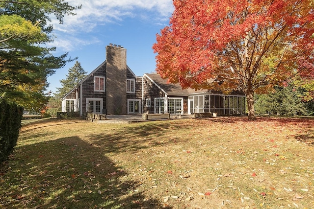 back of property with a sunroom, a chimney, a lawn, and french doors