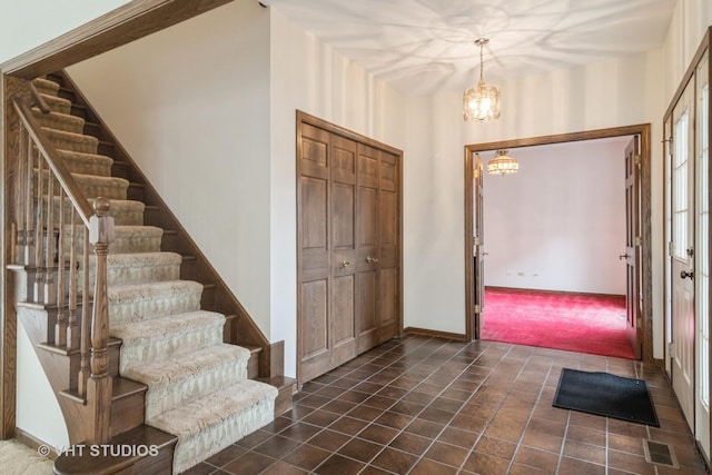 entrance foyer with visible vents, dark tile patterned flooring, stairs, dark colored carpet, and a chandelier