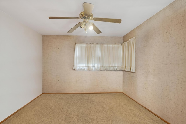 carpeted spare room featuring a ceiling fan, baseboards, and brick wall