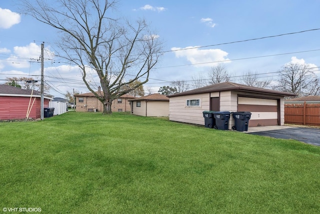 view of yard with a detached garage, fence, and an outbuilding