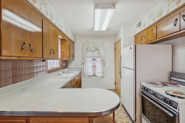 kitchen featuring white range with electric stovetop, light countertops, brown cabinetry, a sink, and a peninsula