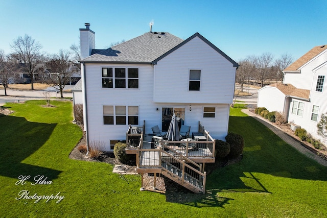 back of property featuring a deck, a yard, roof with shingles, and a chimney