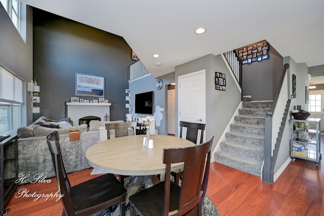 dining room with wood finished floors, recessed lighting, a fireplace, baseboards, and stairs