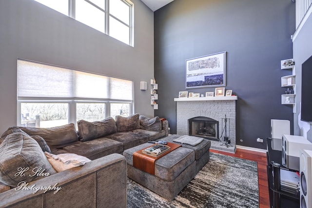 living area with a brick fireplace, wood finished floors, baseboards, and a towering ceiling