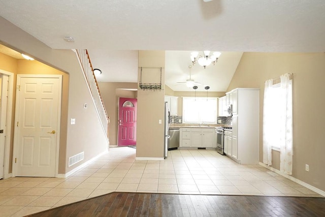 kitchen with lofted ceiling, stainless steel appliances, visible vents, white cabinetry, and tasteful backsplash