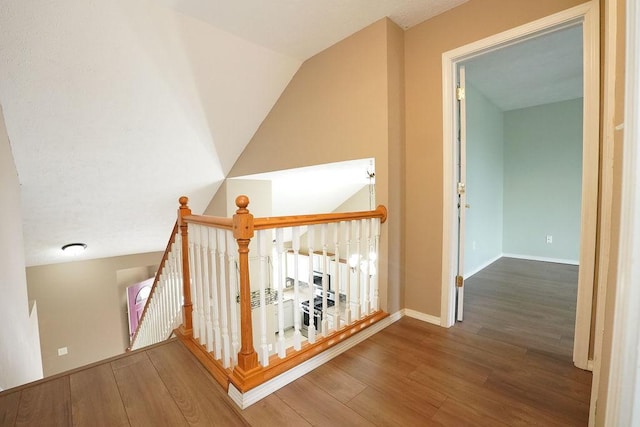 corridor featuring vaulted ceiling, wood finished floors, an upstairs landing, and baseboards