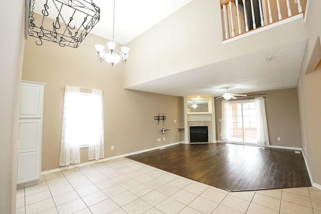 unfurnished living room featuring ceiling fan with notable chandelier, light wood finished floors, a tiled fireplace, and a high ceiling