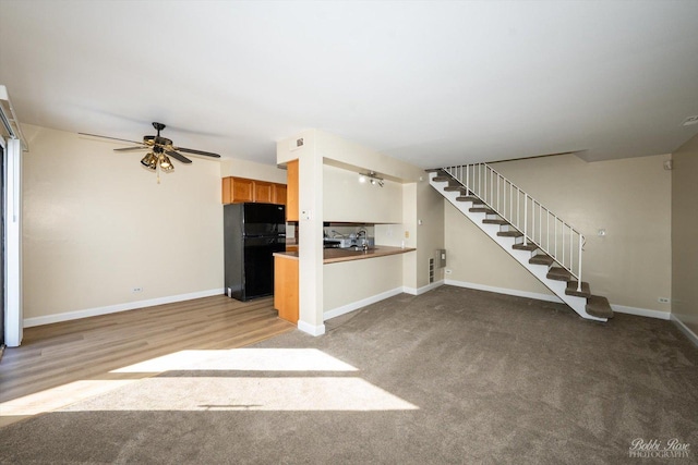 unfurnished living room featuring baseboards, stairway, a ceiling fan, and light colored carpet