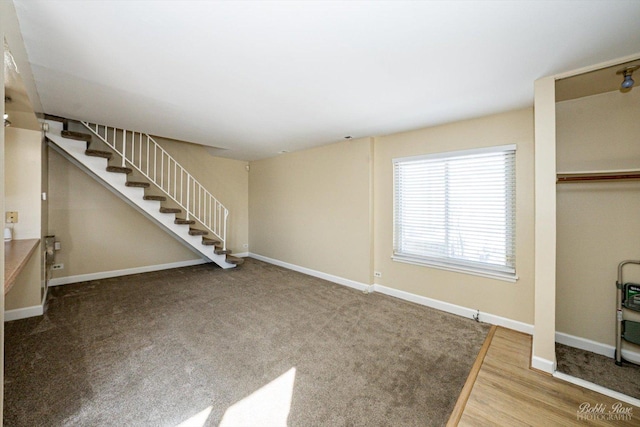 unfurnished living room featuring stairway, wood finished floors, and baseboards