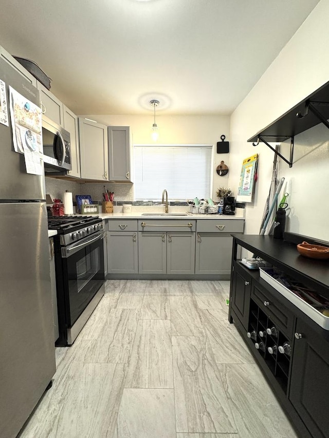 kitchen with stainless steel appliances, decorative backsplash, a sink, and gray cabinetry