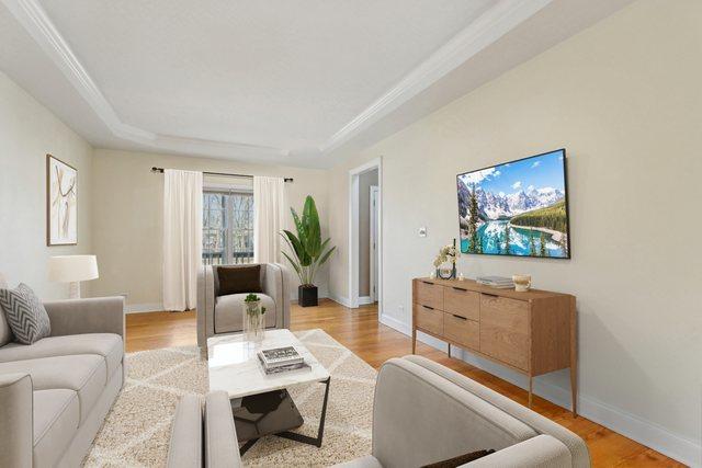 living room featuring a tray ceiling, wood finished floors, and baseboards