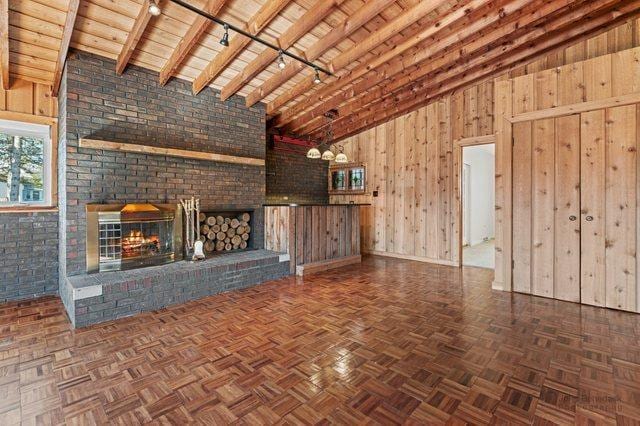 unfurnished living room featuring wooden walls, wooden ceiling, beamed ceiling, rail lighting, and a fireplace