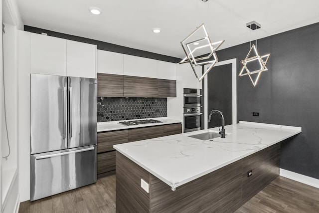 kitchen featuring pendant lighting, stainless steel appliances, white cabinetry, a sink, and modern cabinets