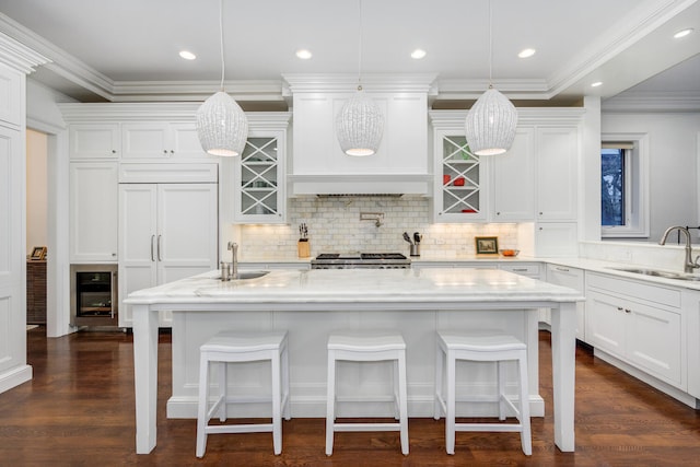 kitchen featuring decorative light fixtures, custom exhaust hood, white cabinetry, a sink, and an island with sink