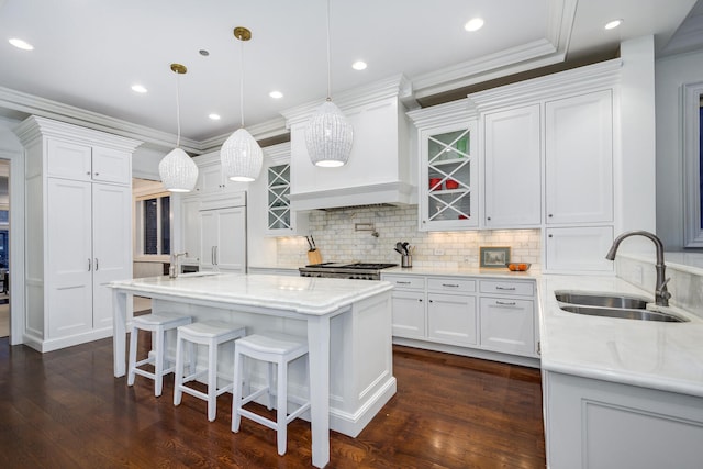 kitchen with pendant lighting, custom exhaust hood, glass insert cabinets, white cabinetry, and a sink