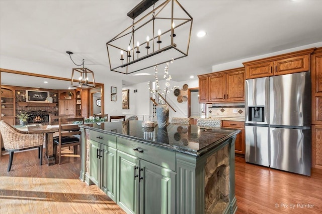 kitchen with pendant lighting, a fireplace, light wood finished floors, backsplash, and stainless steel fridge