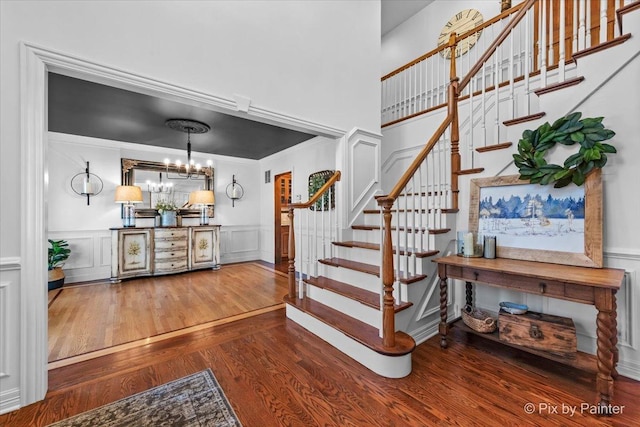 staircase featuring a wainscoted wall, a decorative wall, an inviting chandelier, ornamental molding, and wood finished floors