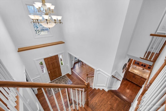 entrance foyer featuring a wainscoted wall, a towering ceiling, an inviting chandelier, wood finished floors, and stairs