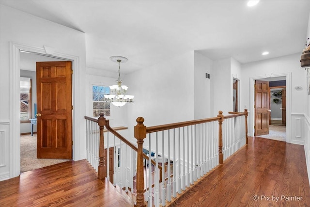 hallway with an inviting chandelier, recessed lighting, wood finished floors, and an upstairs landing