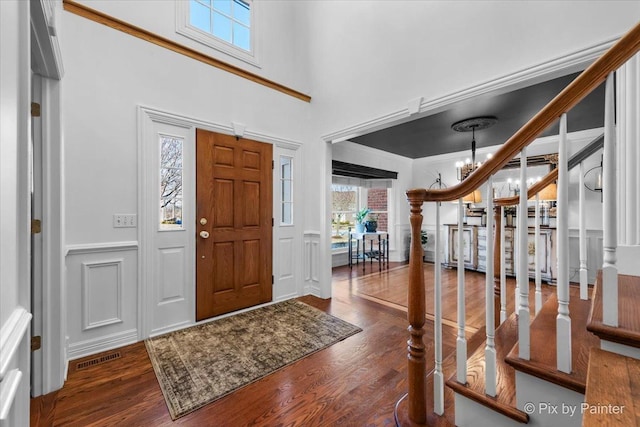 foyer entrance with a wainscoted wall, a decorative wall, a towering ceiling, wood finished floors, and a chandelier