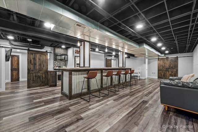 bar featuring visible vents, a barn door, stainless steel range oven, wood finished floors, and black microwave