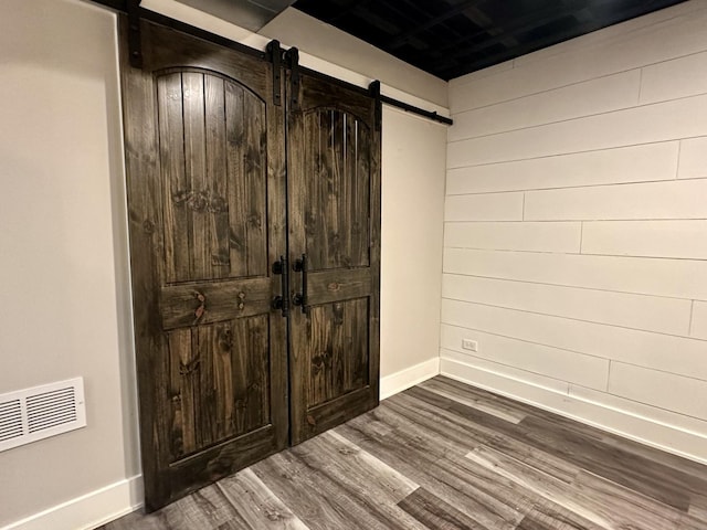 interior space with a barn door, dark wood-type flooring, visible vents, and baseboards