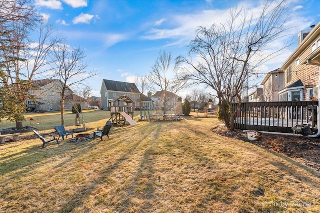 view of yard with a trampoline, an outdoor fire pit, a playground, and a wooden deck