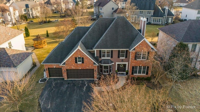 view of front facade with driveway, a residential view, a chimney, roof with shingles, and brick siding