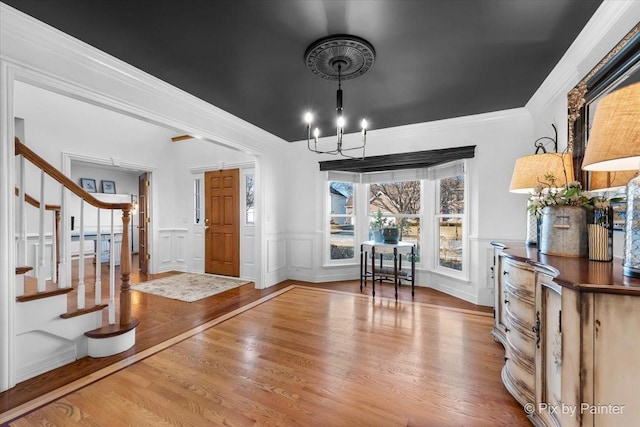 entryway with stairs, ornamental molding, wainscoting, and wood finished floors