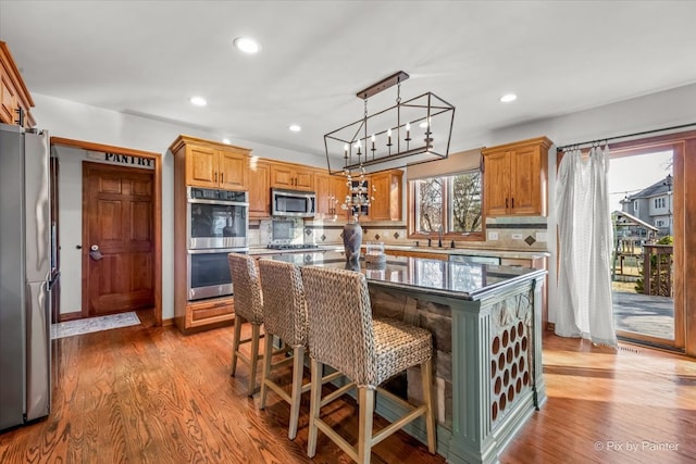 kitchen featuring stainless steel appliances, a breakfast bar, wood finished floors, decorative backsplash, and a center island with sink