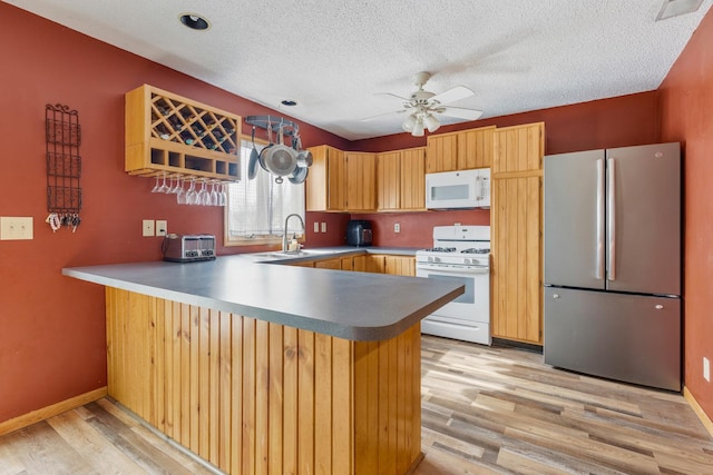 kitchen with a peninsula, white appliances, light wood-style flooring, and a sink