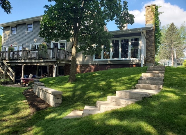 rear view of house with a chimney, a yard, a deck, and stairs