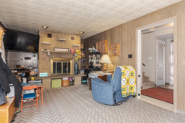 living room featuring a brick fireplace, carpet, wooden walls, and stairway