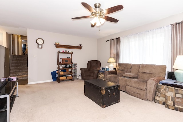 living room with a ceiling fan, light colored carpet, baseboards, and stairs