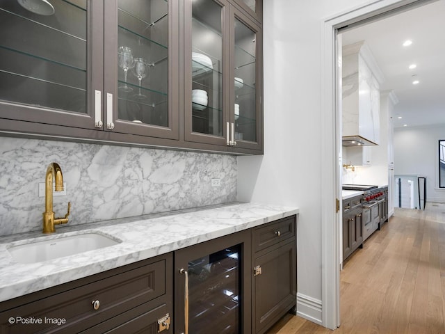 bar featuring light wood-type flooring, beverage cooler, backsplash, and a sink