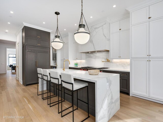 kitchen with hanging light fixtures, white cabinetry, a large island with sink, and light stone countertops