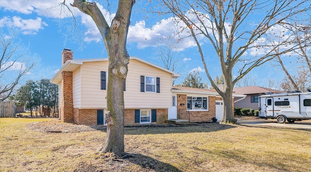 tri-level home featuring a garage, brick siding, a chimney, and a front yard