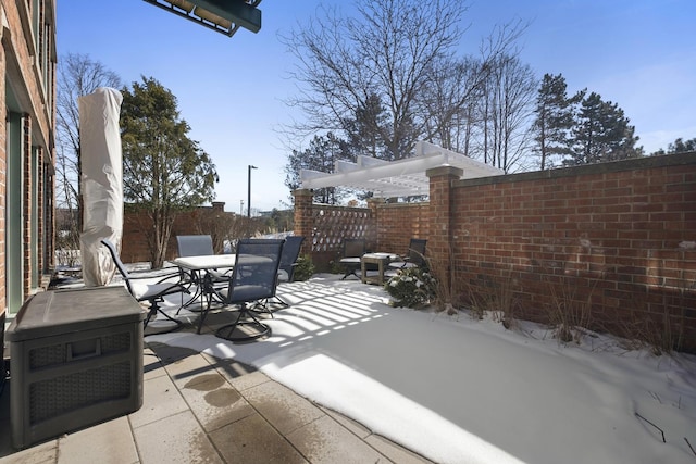 snow covered patio featuring outdoor dining space, fence, and a pergola