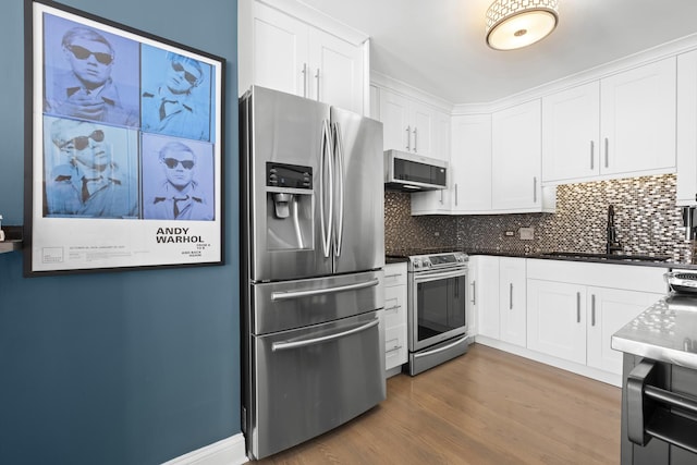 kitchen featuring dark countertops, backsplash, appliances with stainless steel finishes, white cabinets, and a sink