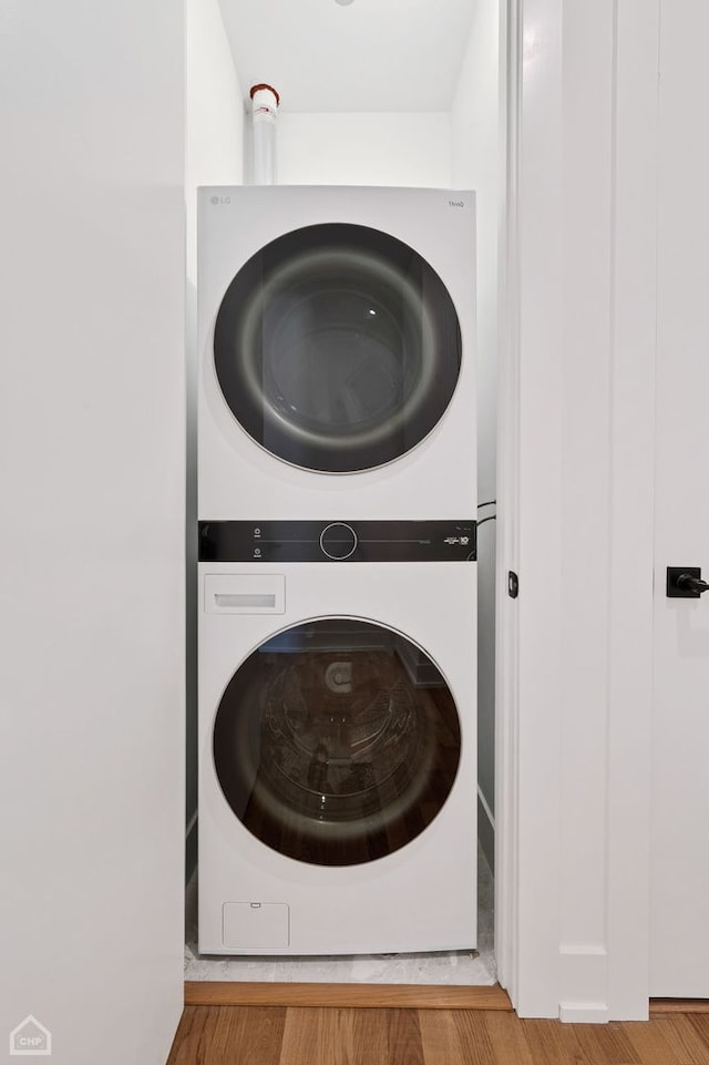 laundry area featuring wood finished floors, stacked washer and clothes dryer, and laundry area