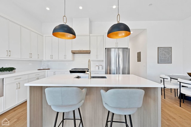 kitchen with an island with sink, white cabinetry, light countertops, and freestanding refrigerator