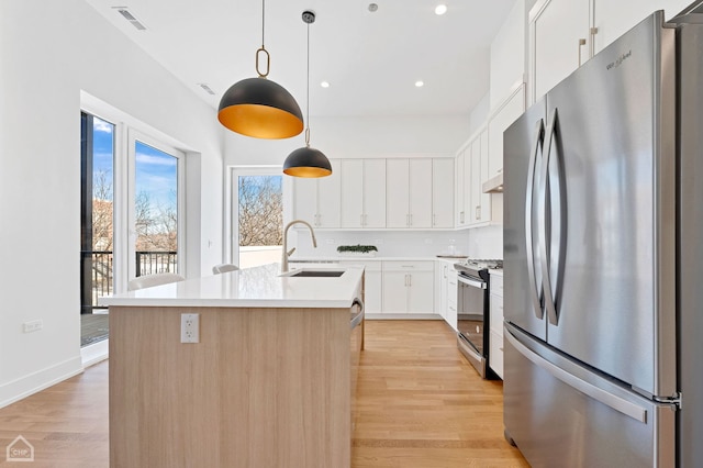 kitchen with a center island with sink, stainless steel appliances, light countertops, white cabinetry, and a sink