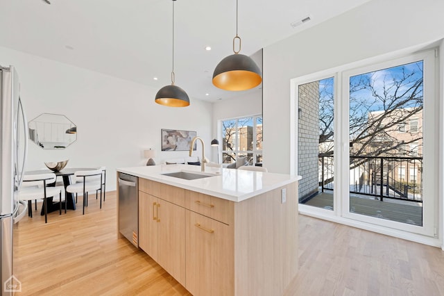 kitchen with a sink, hanging light fixtures, light countertops, appliances with stainless steel finishes, and light brown cabinetry